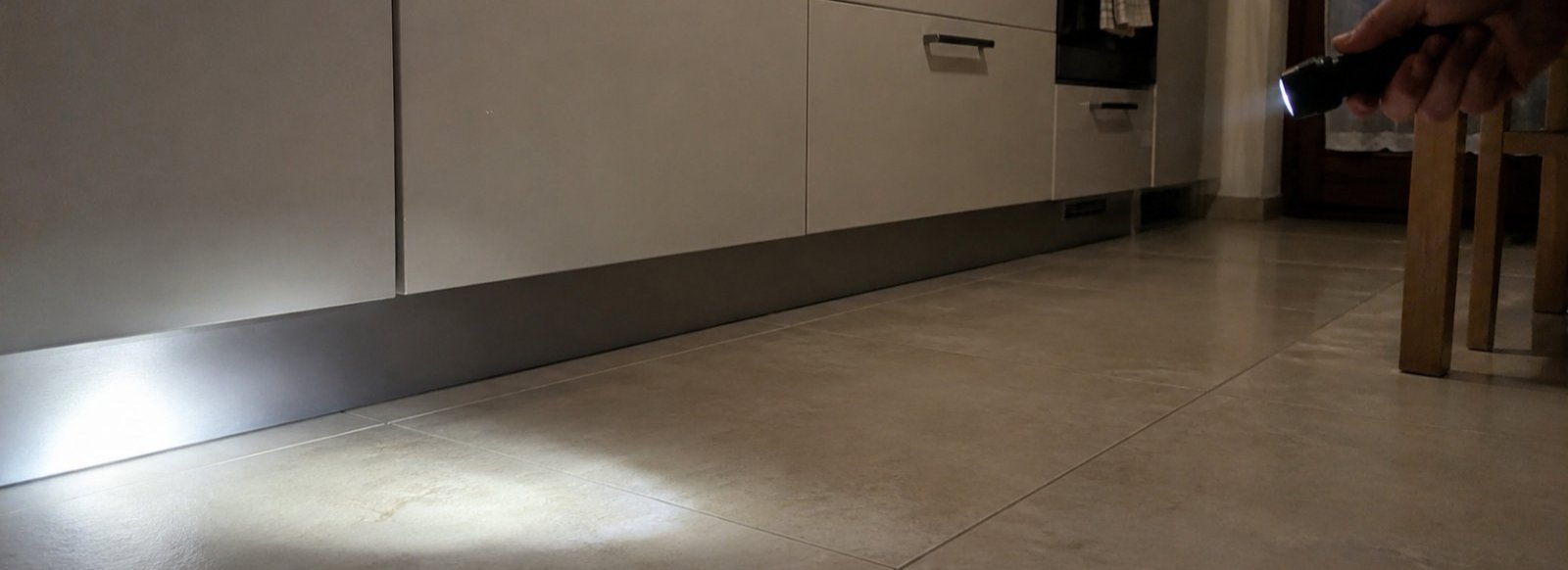 Mano con una torcia che illumina lo spazio sotto un mobile da cucina di sera