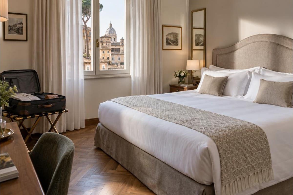 Camera d’albergo nel centro di Roma con valigia aperta e finestra sui tetti