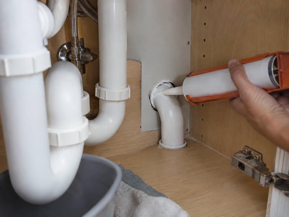 Mano che sigilla con il silicone la fessura attorno a un tubo sotto il lavello