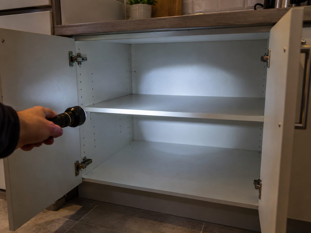 Mano con una torcia che illumina l’interno di un mobile di cucina vuoto