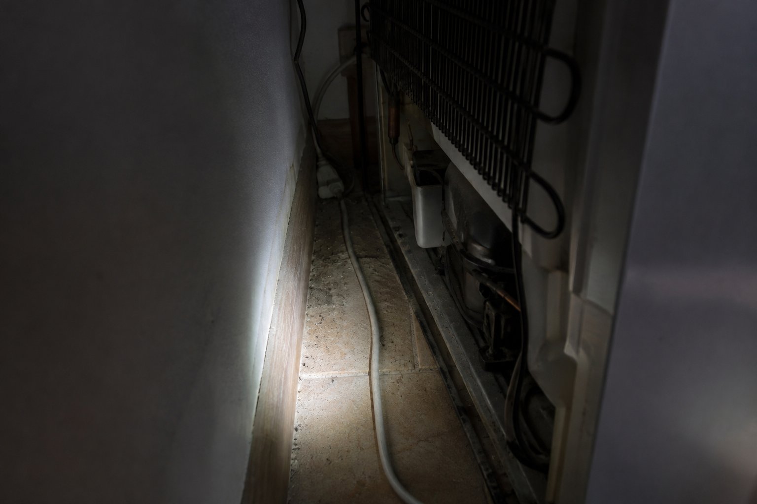Spazio buio dietro un frigorifero illuminato da una torcia