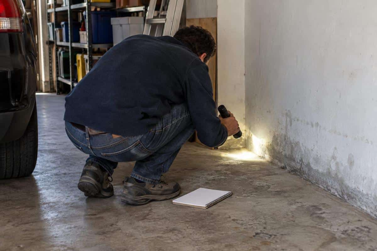 Persona che controlla con una torcia l’angolo fra muro e pavimento in un garage