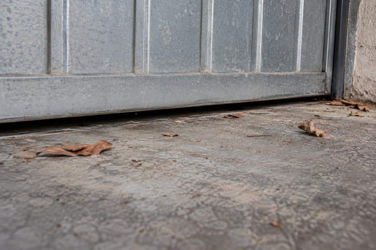 Soglia di una porta basculante di garage con polvere e foglie secche nella fessura sul pavimento