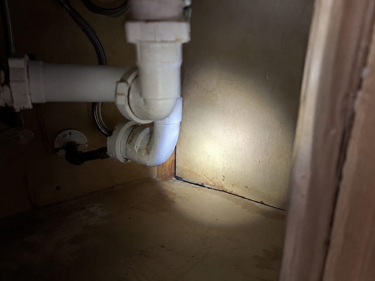 Angolo buio sotto un lavello con tubo di scarico e fessura